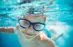 Boy swimming in pool underwater with blue goggles